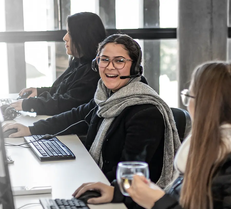 Mulher sorrindo enquanto está sentada em frente ao computador, usando um headset.